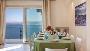 A dining room with a table set for six, overlooking a scenic view of the sea and mountains. - Villa Vista Lago With Pool (Torri del Benaco)