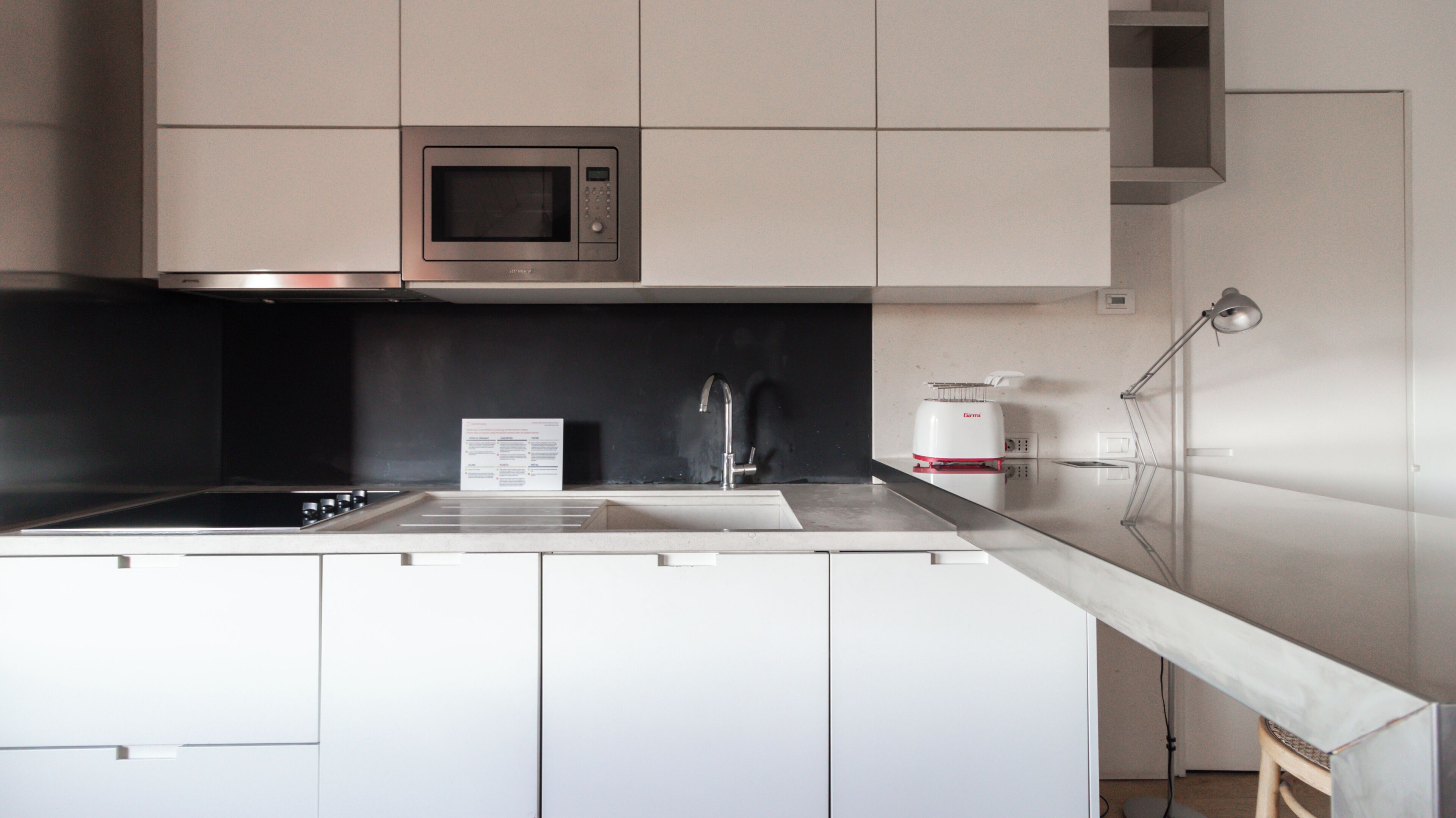 Uma cozinha moderna com micro-ondas integrado, pia de aço inoxidável e cafeteira.