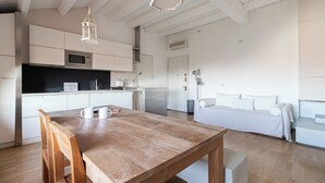 Una cocina moderna con armarios blancos, una mesa de comedor de madera y un sofá blanco en una habitación luminosa con paredes blancas y pisos de madera.