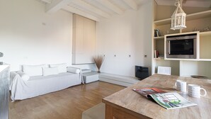 Una sala moderna con un sofá blanco, una mesa de centro de madera y un televisor.