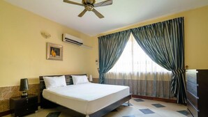 Habitación de hotel con cama, mesita de noche, lámpara, aire acondicionado y cortinas.