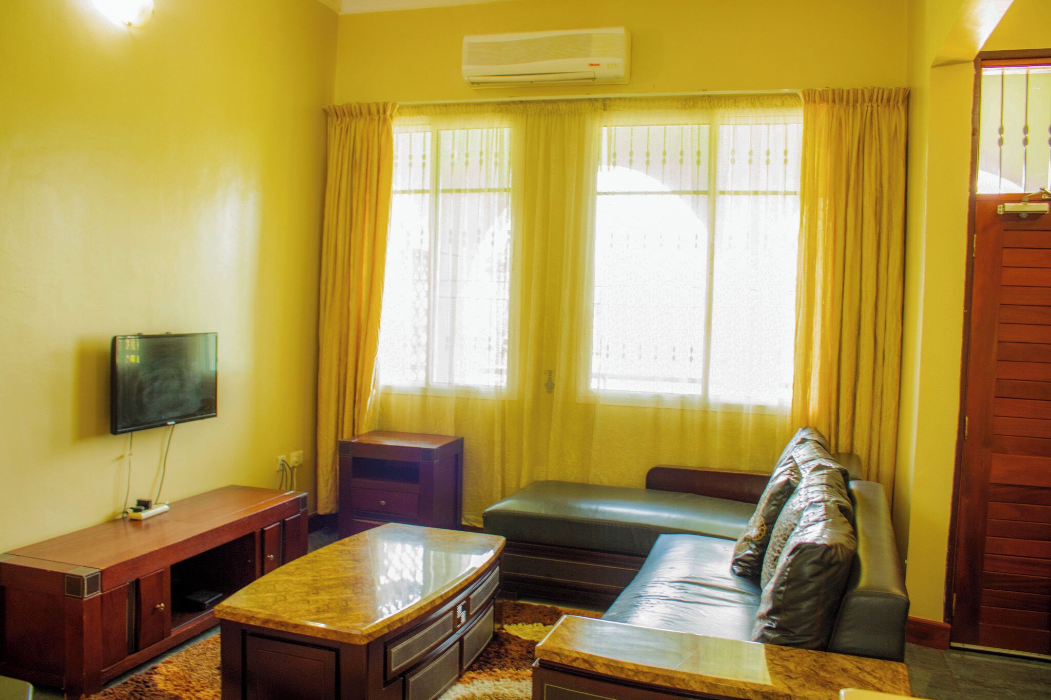 Una sala de estar con un sofá, un televisor montado en la pared y una ventana con cortinas.