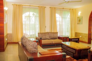 A living room with a sofa, a coffee table, and a TV stand. - Amariah Apartments Bahari Beach (Dar es Salaam)