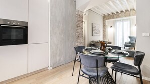 A modern kitchen with white cabinets, a built-in oven, and a dining area with a glass table and grey chairs. - Easylife - Beautiful apartment in Sarpi (Milano)