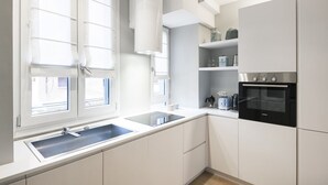 A modern kitchen with white cabinets, a built-in oven, and a window with blinds. - Easylife - Beautiful apartment in Sarpi (Milano)