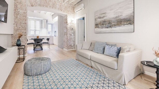 A modern living room with a white sofa, a geometric rug, and a large abstract painting on the wall. - Easylife - Beautiful apartment in Sarpi (Milano)