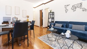 Una sala moderna con un sofá azul, una mesa de comedor con sillas y un televisor.