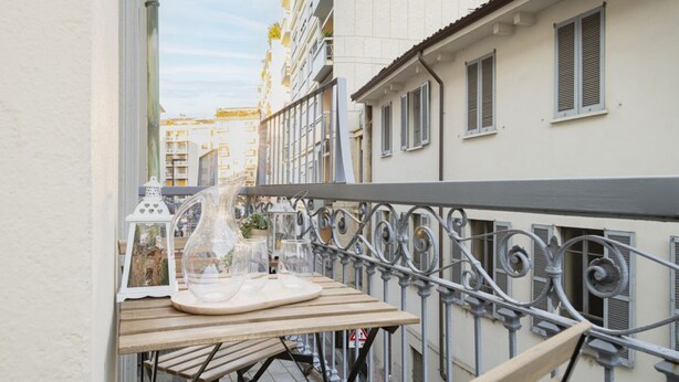 Un balcón con una mesa dispuesta para dos, que incluye un jarrón de vidrio transparente y un cuadro enmarcado.
