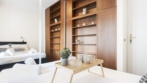 Habitación de hotel con cama, mesita de noche con bandeja, una estantería de madera grande y una puerta blanca.