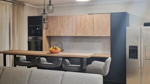 Une cuisine moderne avec des meubles en bois, un réfrigérateur en acier inoxydable et un coin repas comprenant un canapé et des chaises gris.