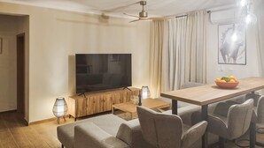 Un salon moderne doté d’un téléviseur à écran plat, de meubles en bois, d’une table à manger avec des chaises et d’un ventilateur de plafond.