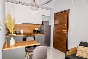 Une cuisine compacte dotée d’un plan de travail en bois, d’un réfrigérateur en acier inoxydable et d’un luminaire suspendu au design moderne.