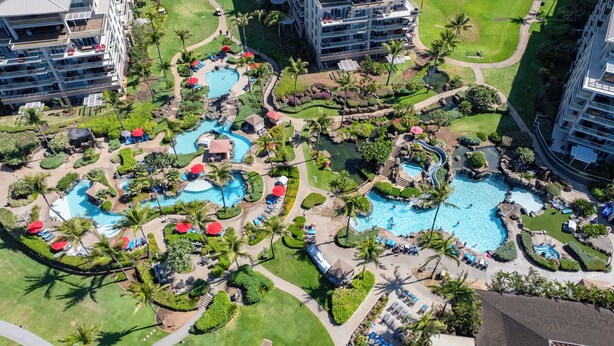 Eine Vogelperspektive auf ein Resort mit mehreren Swimmingpools, Palmen und einem gepflegten Rasen.