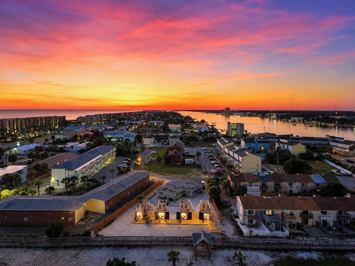 Una cittadina costiera al tramonto, con un porto turistico, edifici residenziali e una spiaggia sabbiosa con una piccola costruzione.
