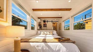 A bedroom with a large bed, a bedside lamp, and a wooden nightstand. - Tiny Beach Boardwalk Bungalow D | Rooftop Retreat (Fort Walton Beach)