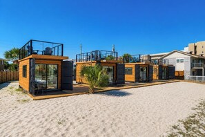 A beachfront property with multiple wooden cabins, each featuring a balcony and a sliding door. - Tiny Beach Boardwalk Bungalow D | Rooftop Retreat (Fort Walton Beach)
