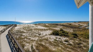 A beach view with a wooden walkway leading to the water, sandy dunes, and a clear blue sky. - Tiny Beach Boardwalk Bungalow D | Rooftop Retreat (Fort Walton Beach)
