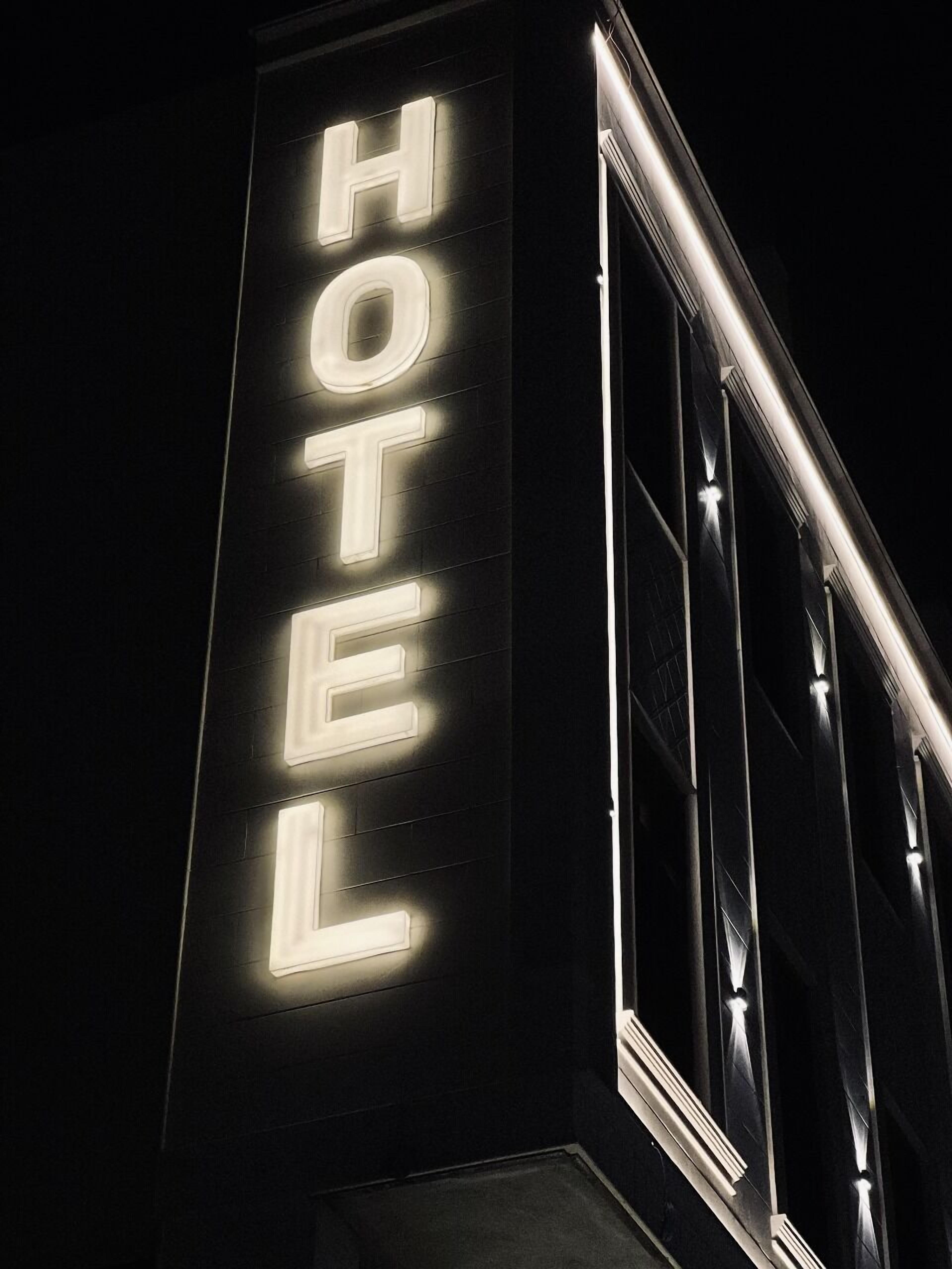 Une enseigne d’hôtel avec des lettres lumineuses épelant le mot «HÔTEL» sur la façade sombre d’un immeuble.