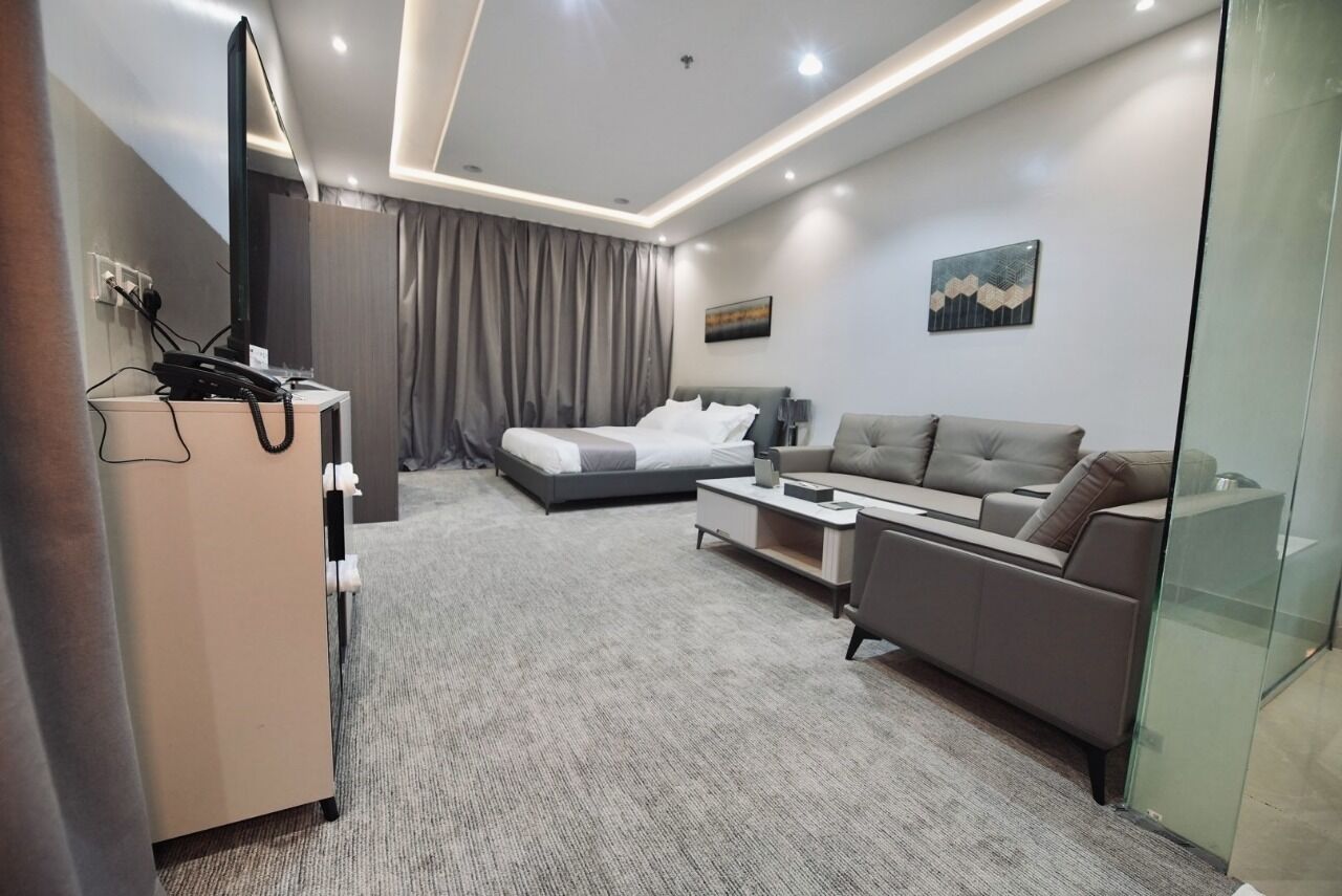 A modern hotel room with a bed, a sofa, a desk, and a glass partition.