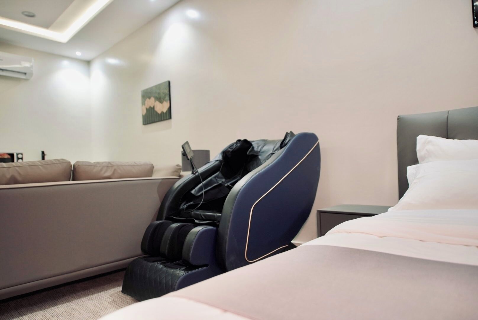 Un dormitorio moderno con una silla de masajes, una cama, un sofá y un aire acondicionado instalado en la pared.