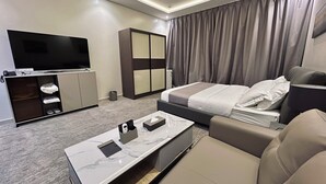 A modern hotel room with a flat-screen TV, a sofa, a bed, a minibar, and a large window with curtains. - qimampark albaha7 (Al Baha)