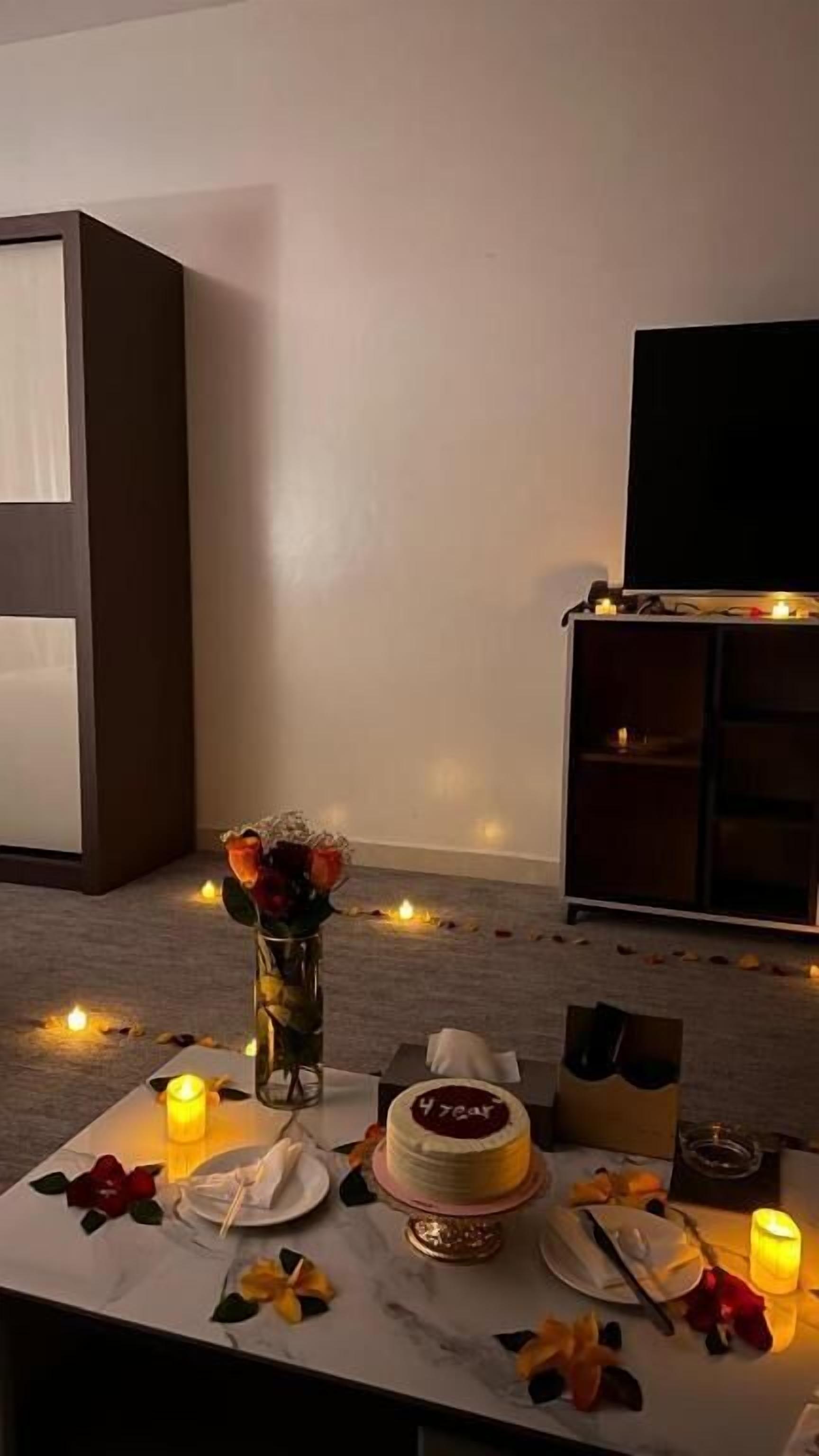 A dining table set with candles, a cake, and a vase of flowers.