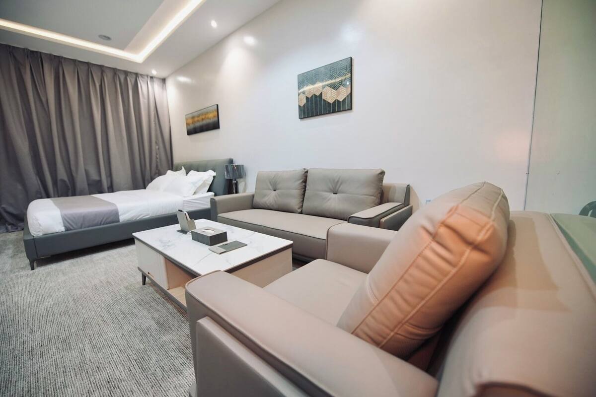 A hotel room with a bed, two sofas, a coffee table, and two paintings on the wall.