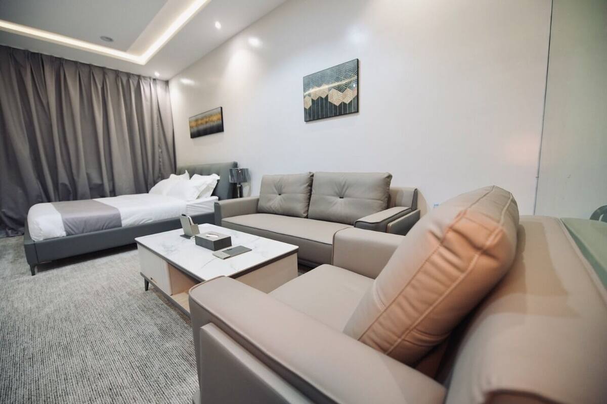 A modern hotel room with a bed, a sofa, a coffee table, and a desk.