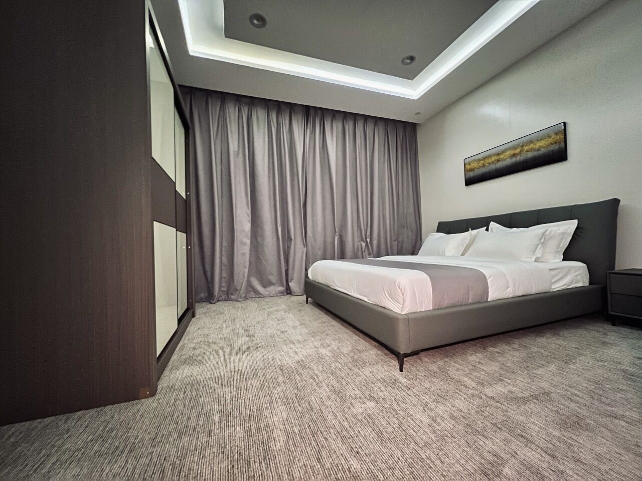 Een moderne hotelkamer met een groot bed, nachtkastje, kledingkast en een plafondlamp.