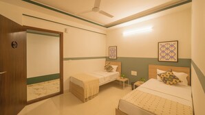 Una habitación de hotel con dos camas, un ventilador de techo, una mesita de noche con lámpara y un espejo.