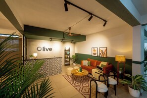 A modern living room with a sofa, coffee table, and chairs. There is a 'live' sign on the wall, a bookshelf, and a plant. - Olive Mahalakshmi Metro by Embassy Group (Bengaluru)
