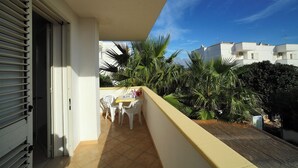 A balcony with a table and chairs, surrounded by greenery and buildings in the background. - Vacation Home Aphrodite Torre Mozza (Torre Mozza)