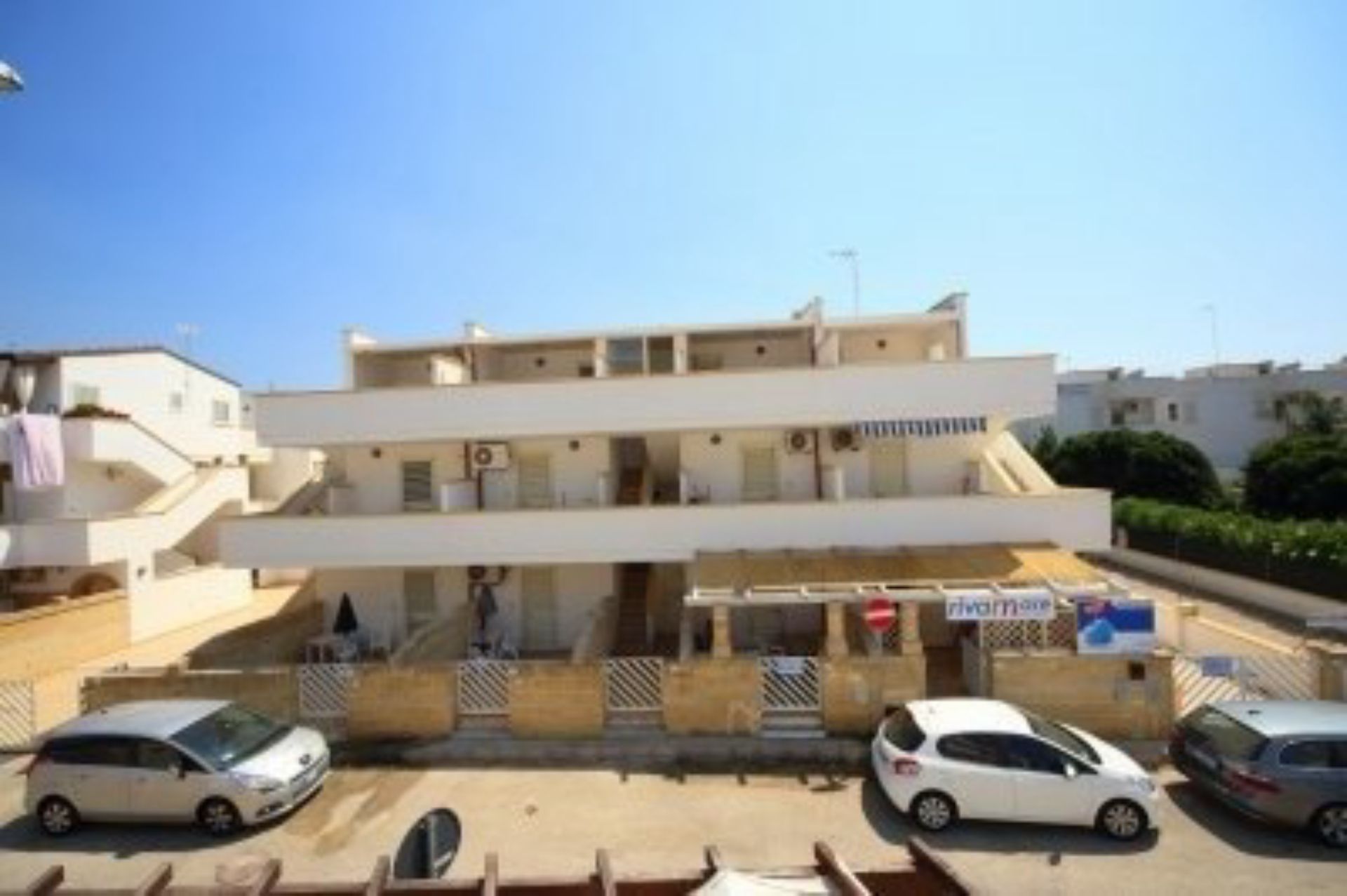 Un edificio de varios pisos con techo plano, zona de estacionamiento techada y escaparate visible.