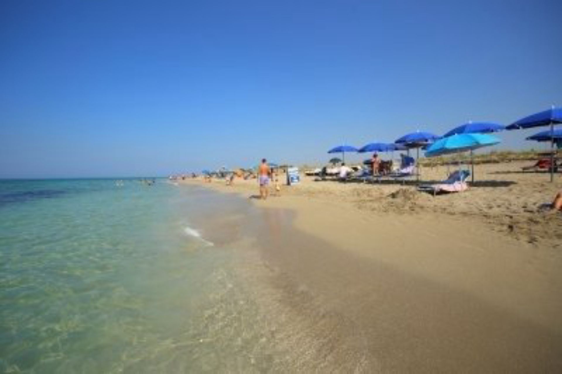Una spiaggia con acqua cristallina, ombrelloni e lettini.