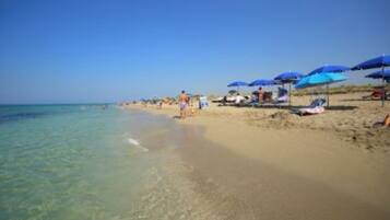 Una spiaggia con acqua cristallina, ombrelloni e lettini.