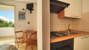A compact kitchen with a gas stove, sink, and wooden chairs. A small table is placed near the window, and a poster is visible on the wall. - Vacation Home Aphrodite Torre Mozza (Torre Mozza)