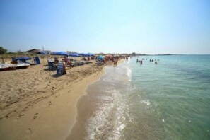 Una playa con agua cristalina, sombrillas y gente.
