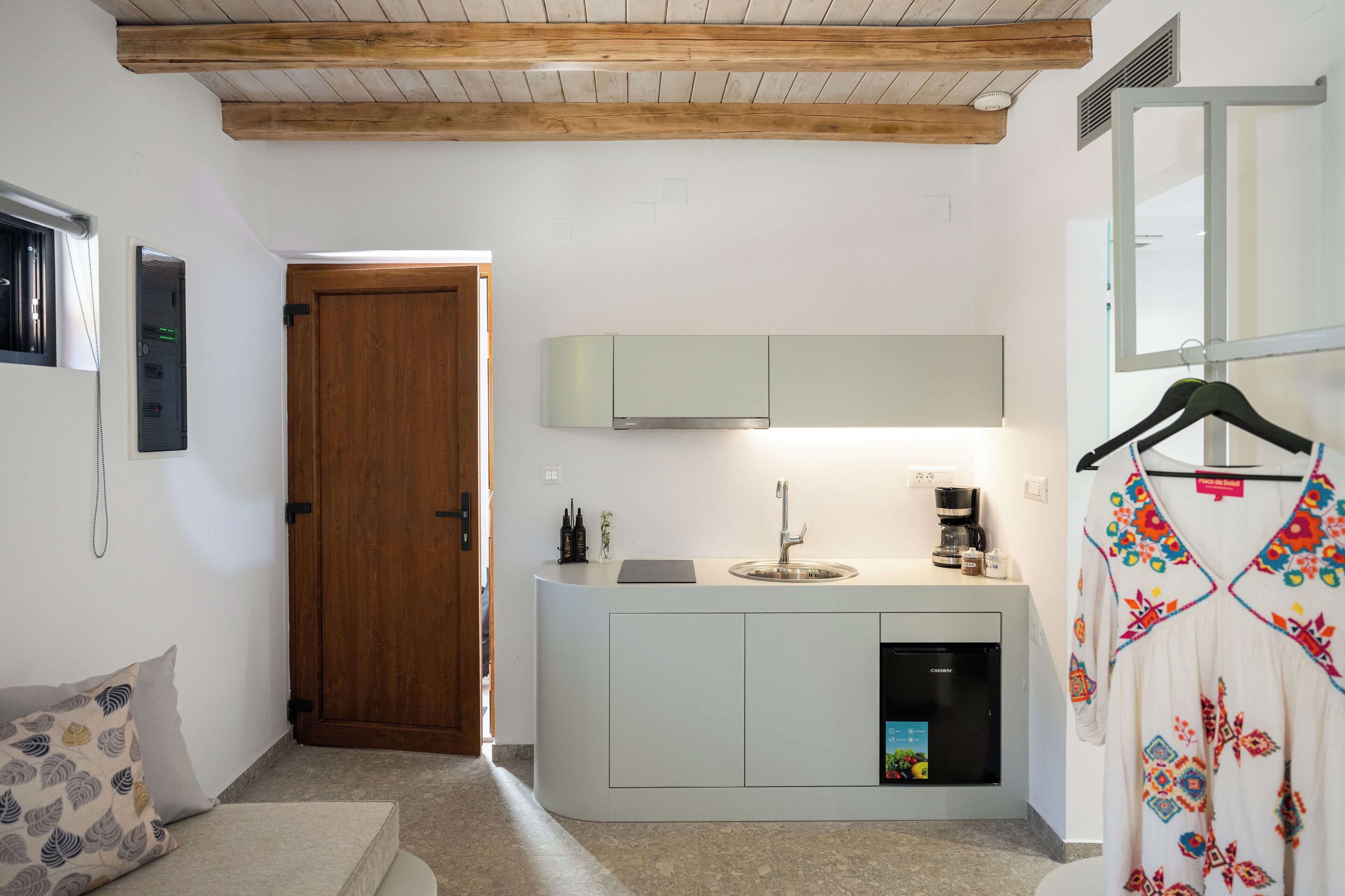 A compact kitchen with a built-in dishwasher, a wooden door, and a hanging garment.