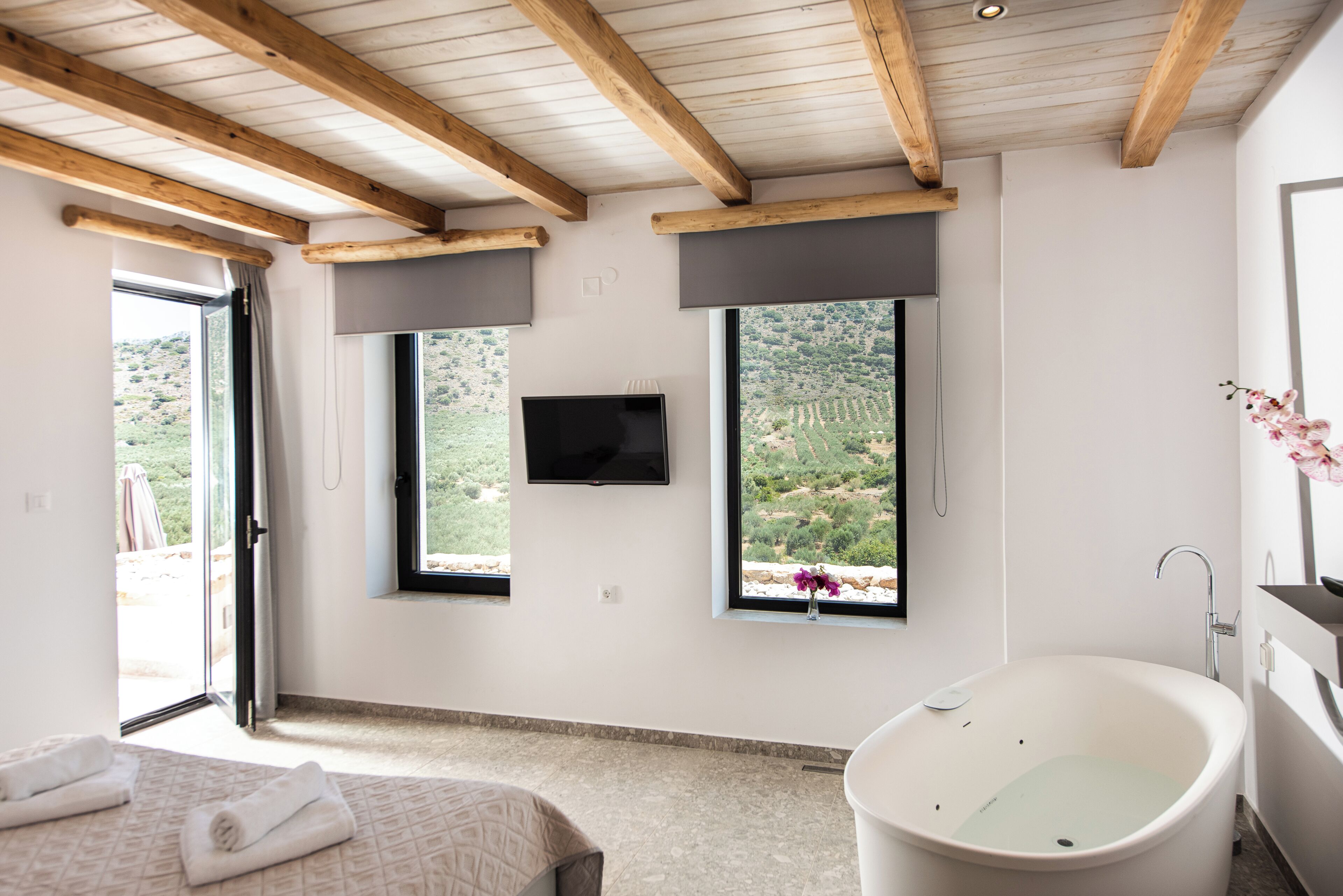 A bedroom with a bed, a bathtub, and two windows with views of a landscape.