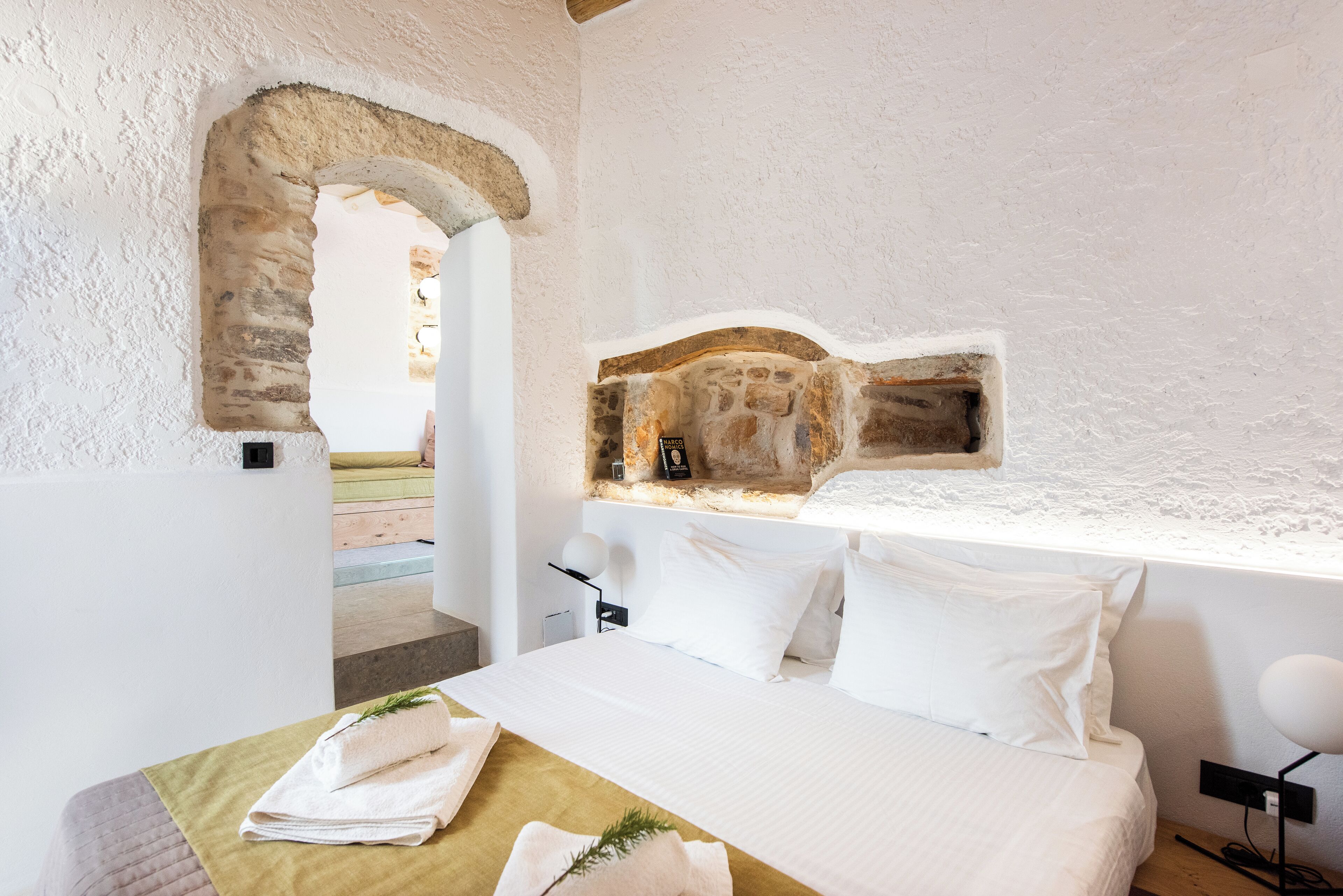 Un dormitorio con un arco de piedra, una cama con sábanas blancas y una repisa de piedra sobre la cama.
