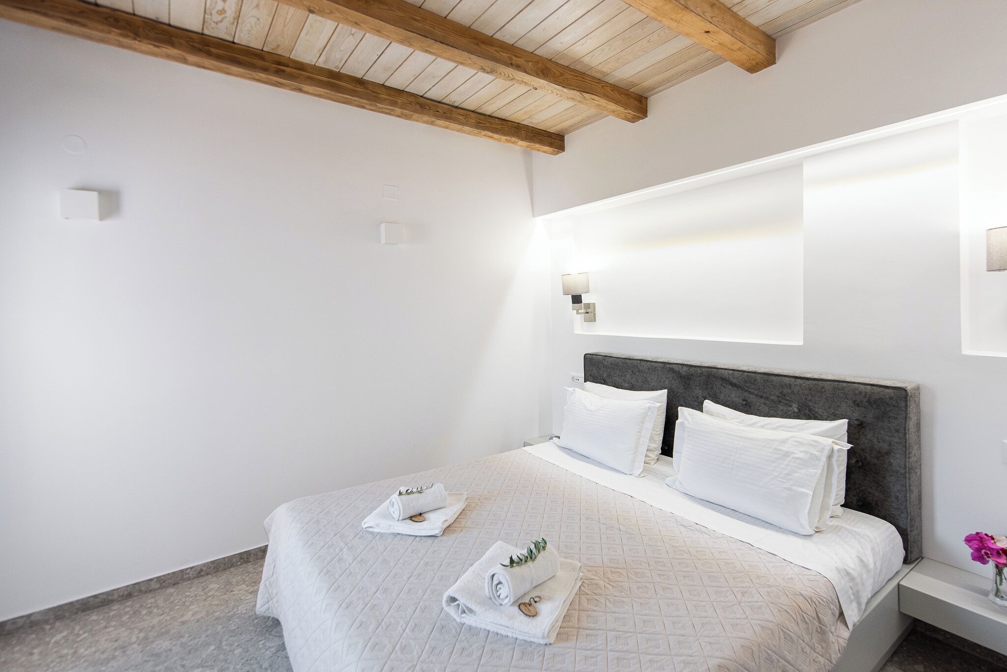 Una cama bien hecha con sábanas y toallas blancas, una viga de techo de madera y un aplique de pared.