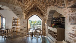 Un intérieur rustique en pierre, avec un coin repas, des meubles en bois et une vue dégagée sur l’extérieur, accessible par une arche.