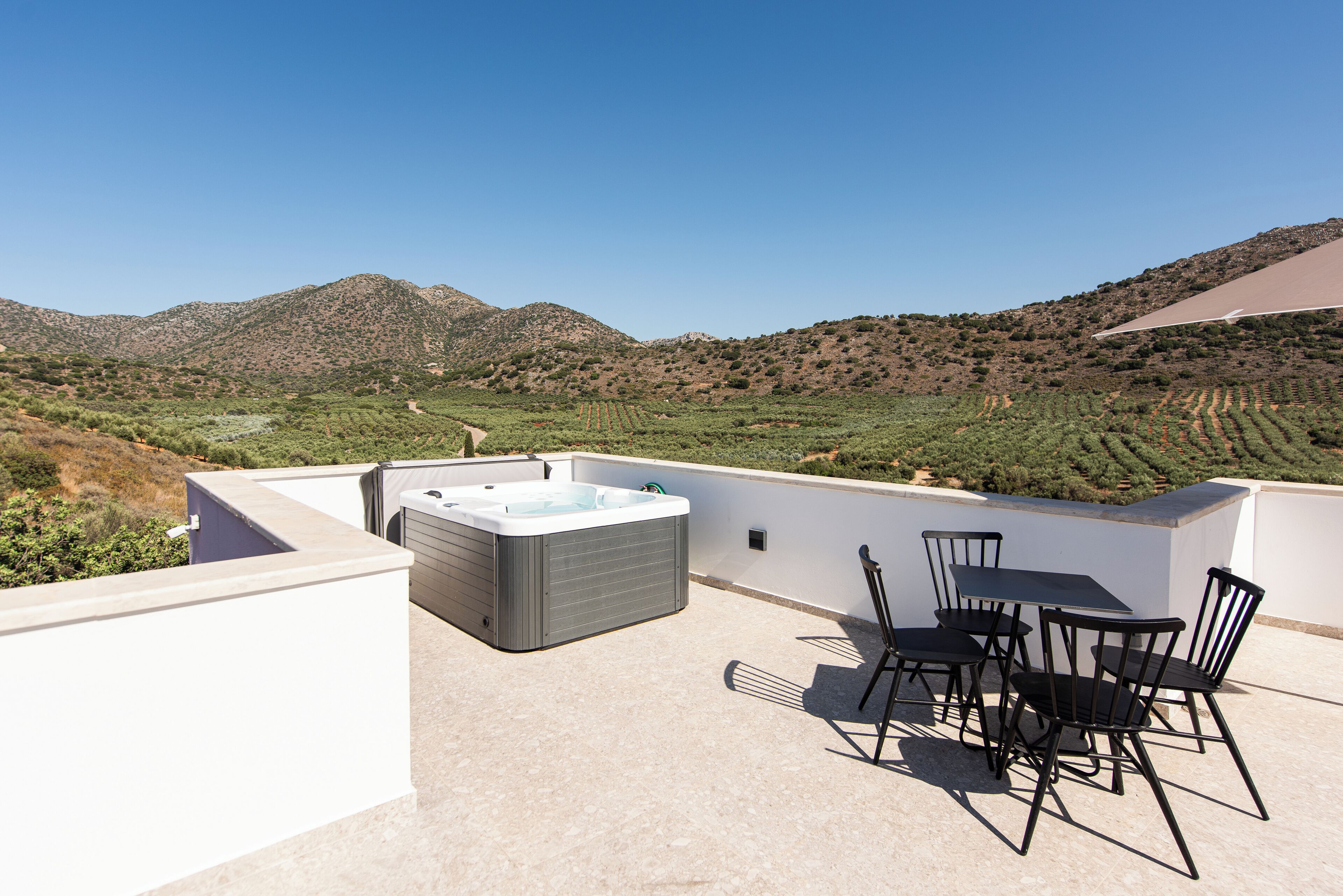 Une terrasse sur le toit avec un jacuzzi, des sièges d’extérieur et une vue sur un vignoble et des collines.