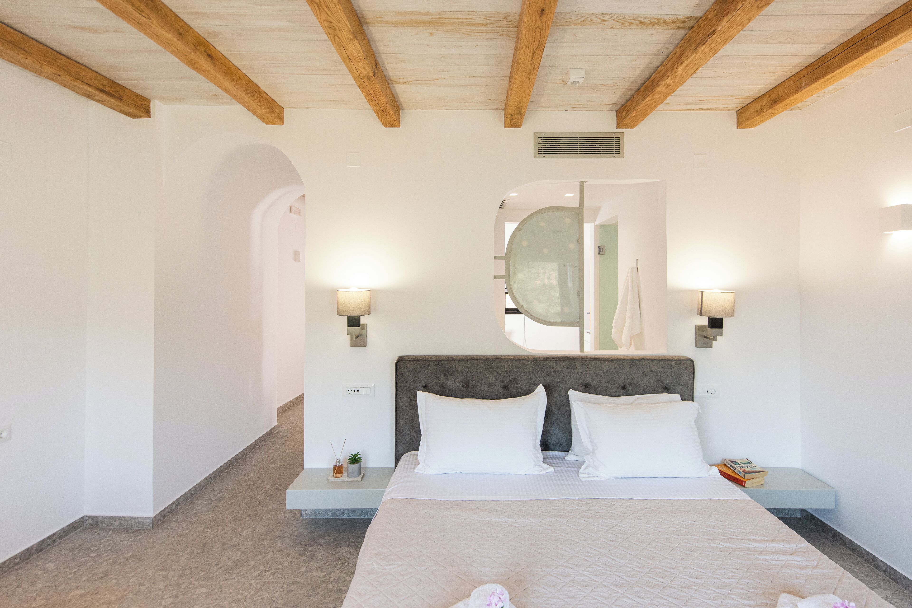 A bedroom with a large bed, two bedside tables, a wall-mounted mirror, and a ceiling fan.