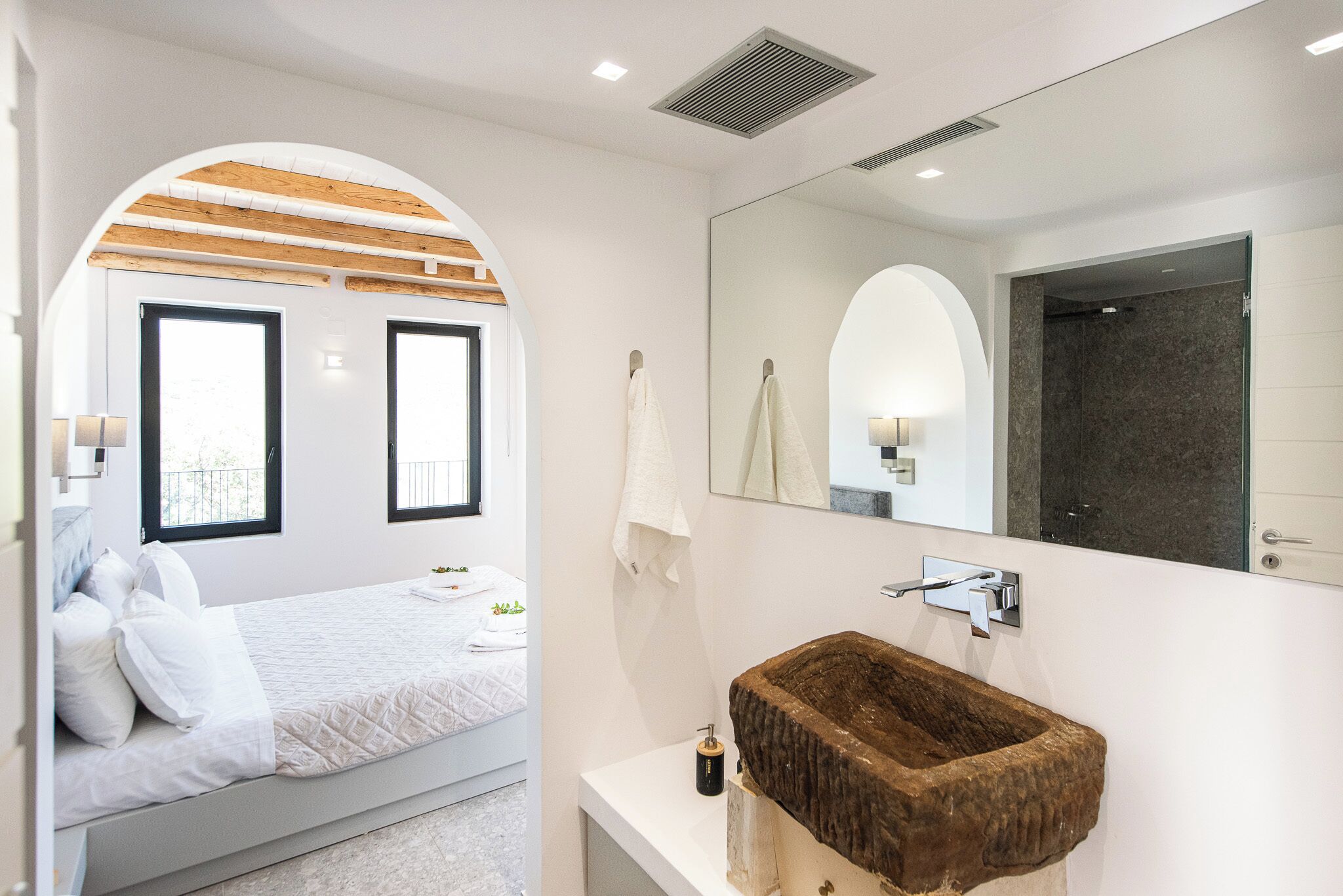 Een moderne slaapkamer met een bed, een grote spiegel en een bijzondere wastafel van steen.