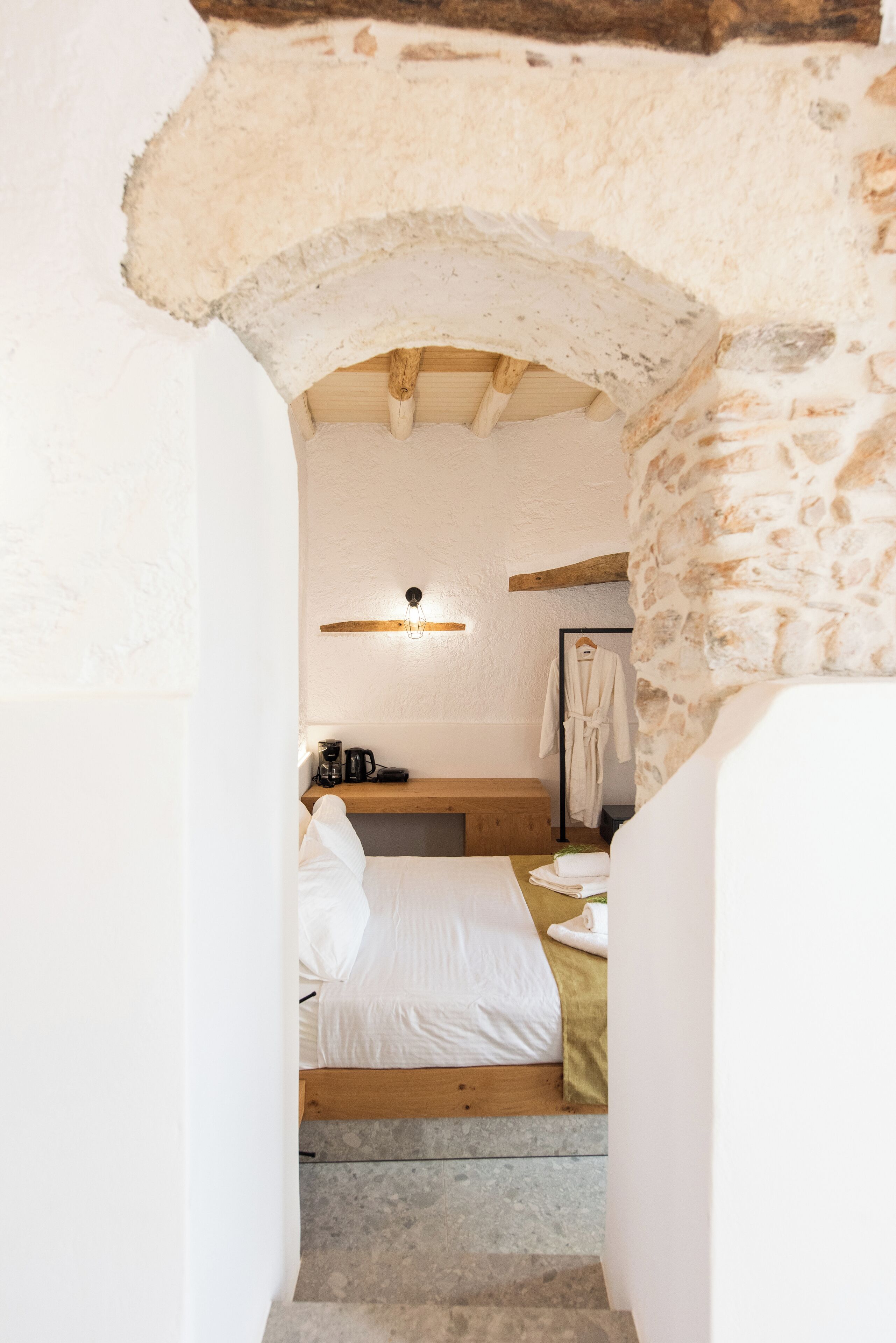 Un dormitorio acogedor con pared de piedra, cama de madera, mesita de noche con lámpara y bata colgada en un perchero.