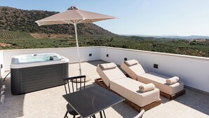 Une terrasse sur le toit équipée d’un jacuzzi, de deux chaises longues, d’une table et d’un parasol.
