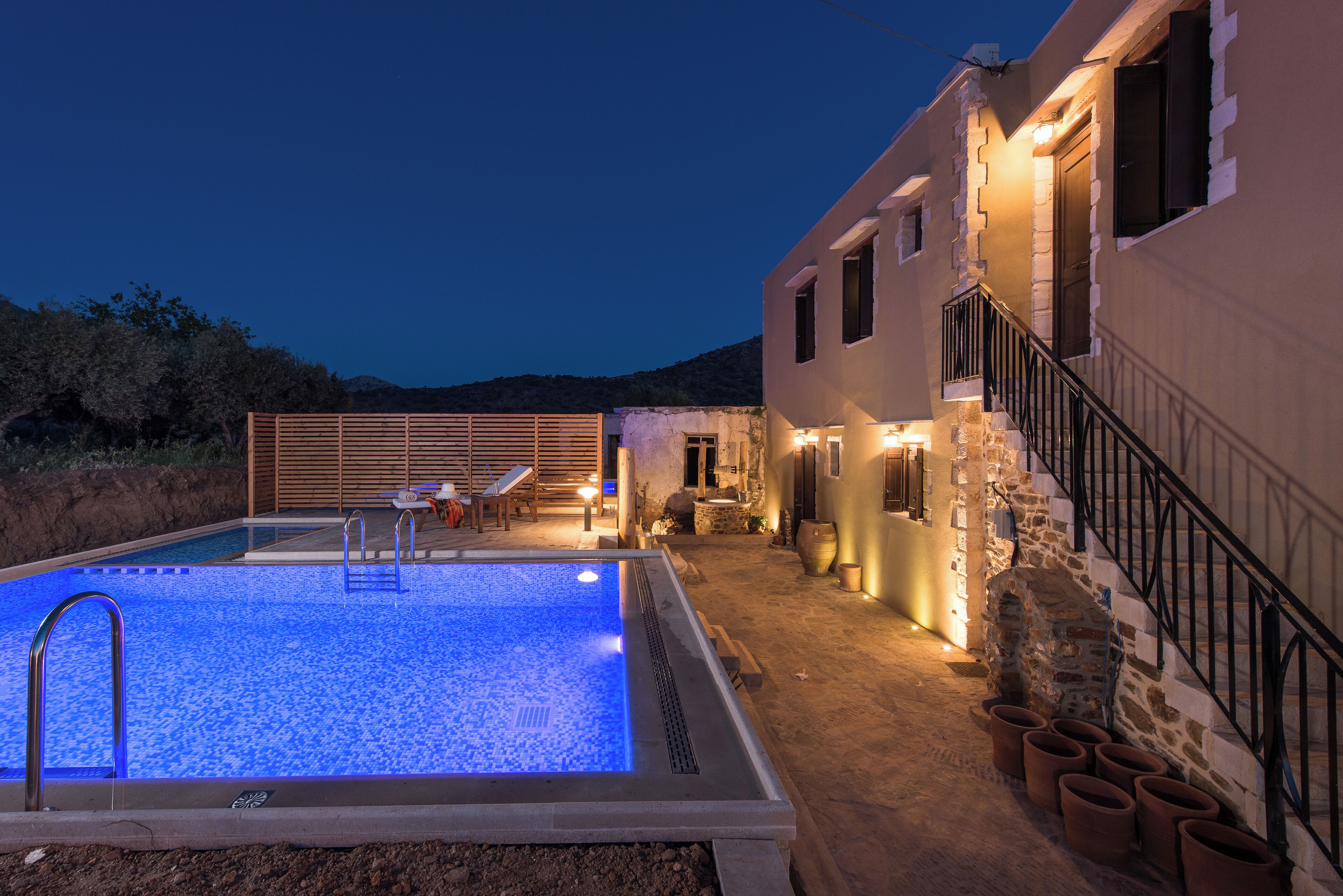 Piscina com muro de pedra e escadaria que leva a um edifício.