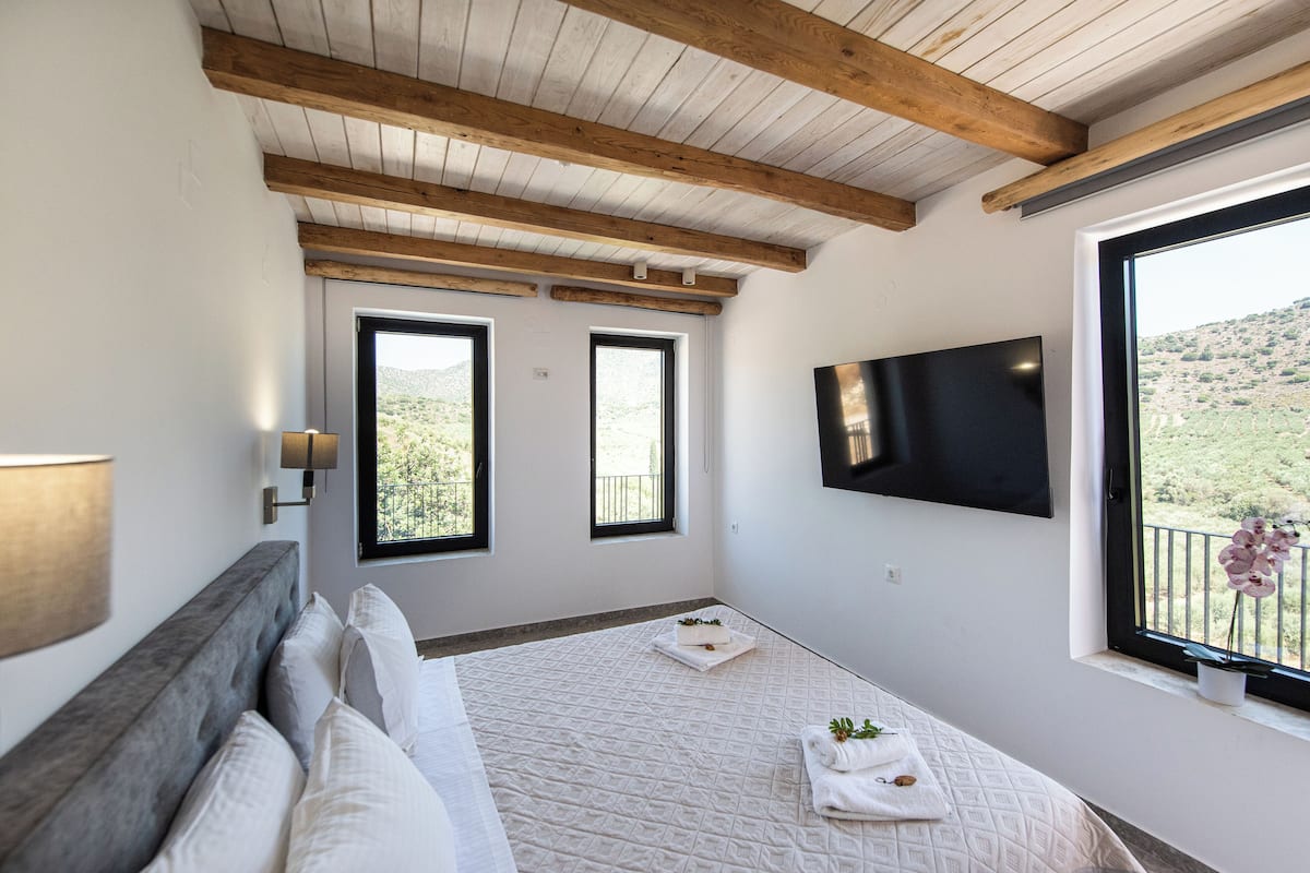 Een slaapkamer met een bed, een aan de muur bevestigde televisie en een raam met uitzicht op het omliggende landschap.