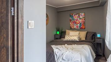 Et soveværelse med en seng, et natbord med lampe, et vægur og et billede.